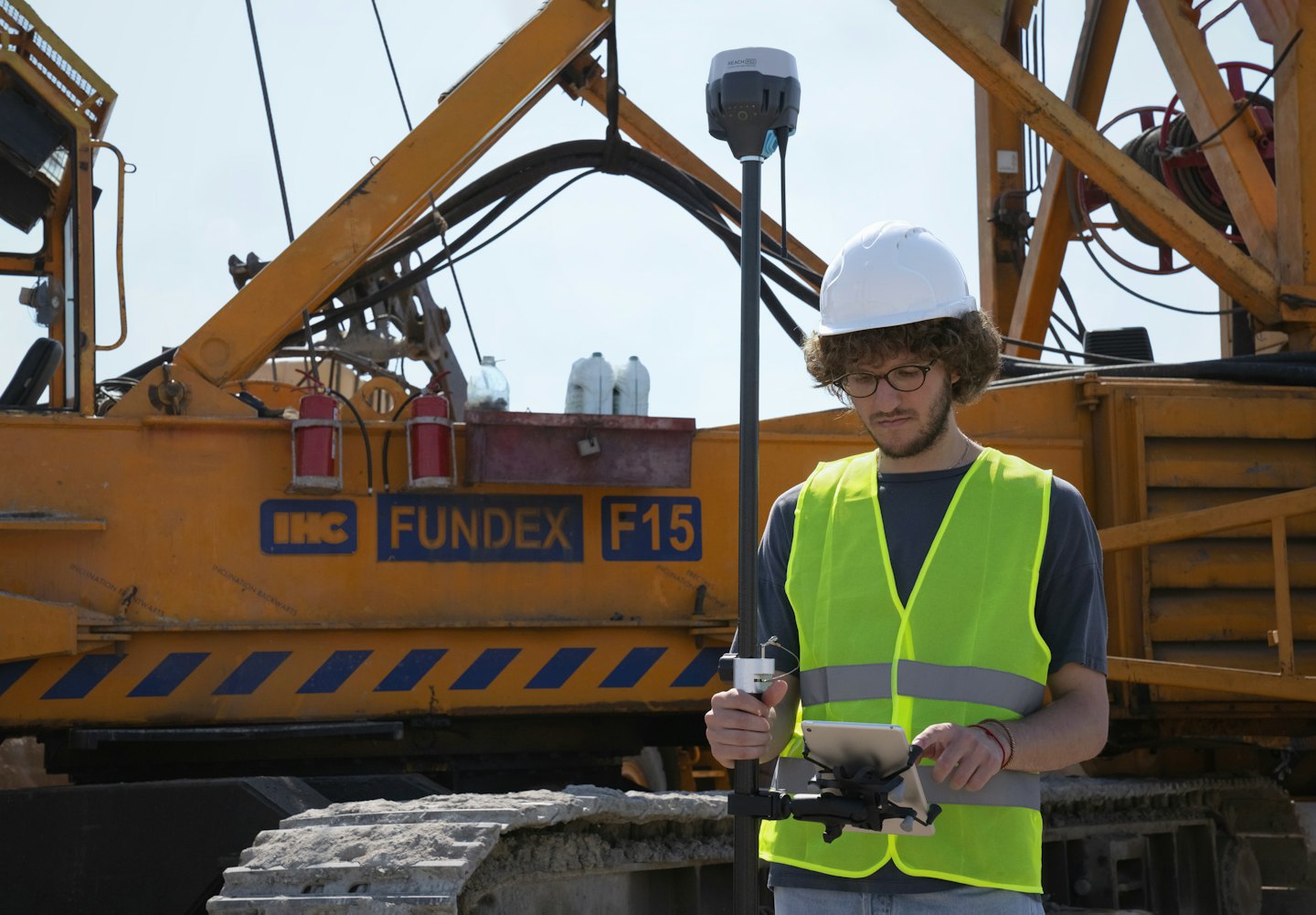 Surveyor uses tablet on construction site with heavy machinery.