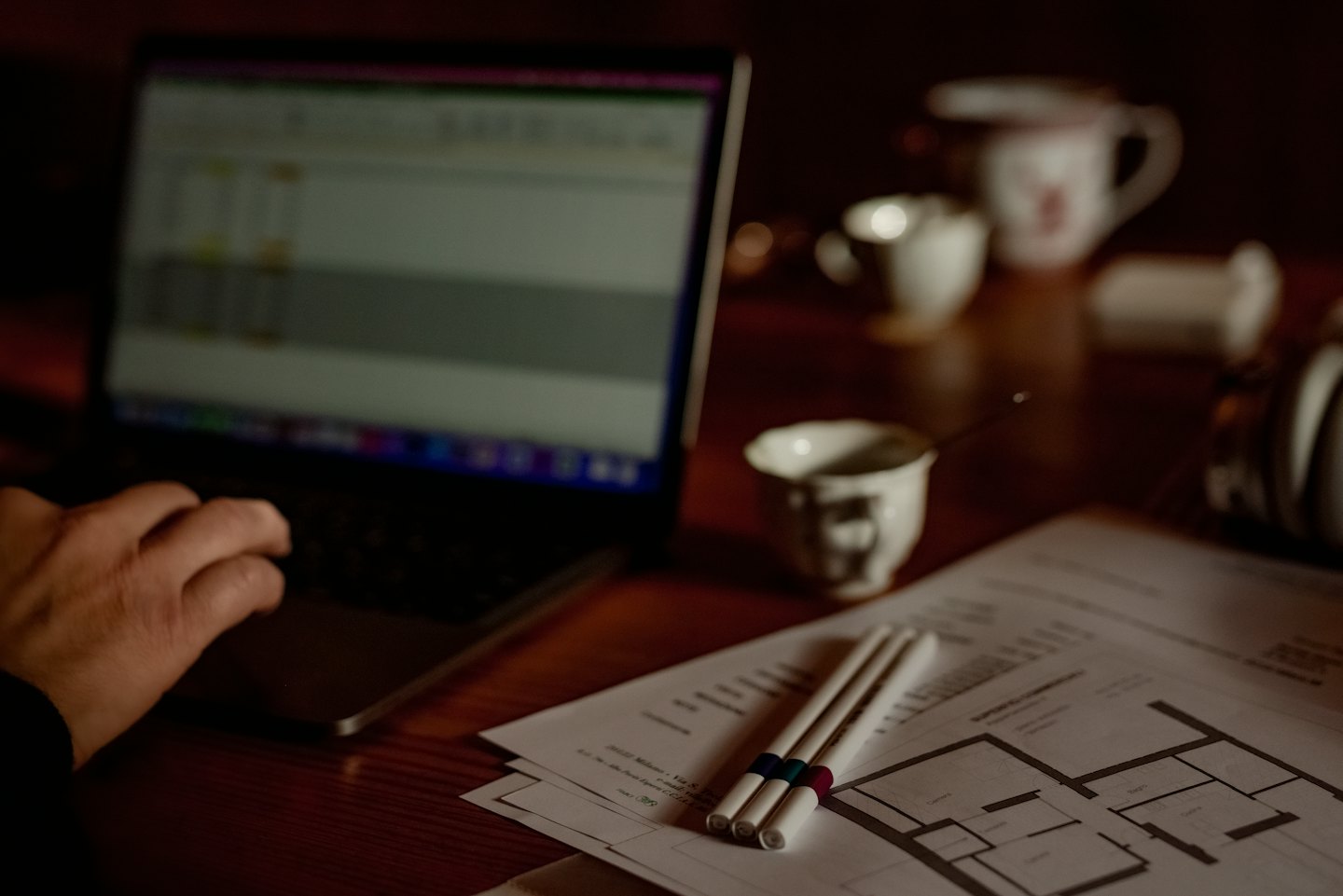 Hand typing on laptop next to architectural plans and proposal document.